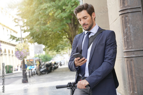 Businessman in the street using smartphone and electric scooter