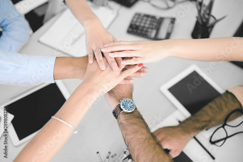 Closeup of business team putting their hands on top of each other. Group of happy business people holding hands together while sitting around the desk.