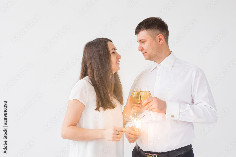 New year, holidays, date and valentines day concept - Loving couple holding sparklers light and glasses of champagne over white background New year, holidays, date and valentines day concept - Loving couple holding sparklers light and glasses of champagne over white background
