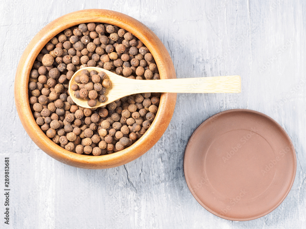 Allspice (Jamaica pepper) in a wooden cup with spoon and clay plate on a gray background Allspice (Jamaica pepper) in a wooden cup with spoon and clay plate on a gray background