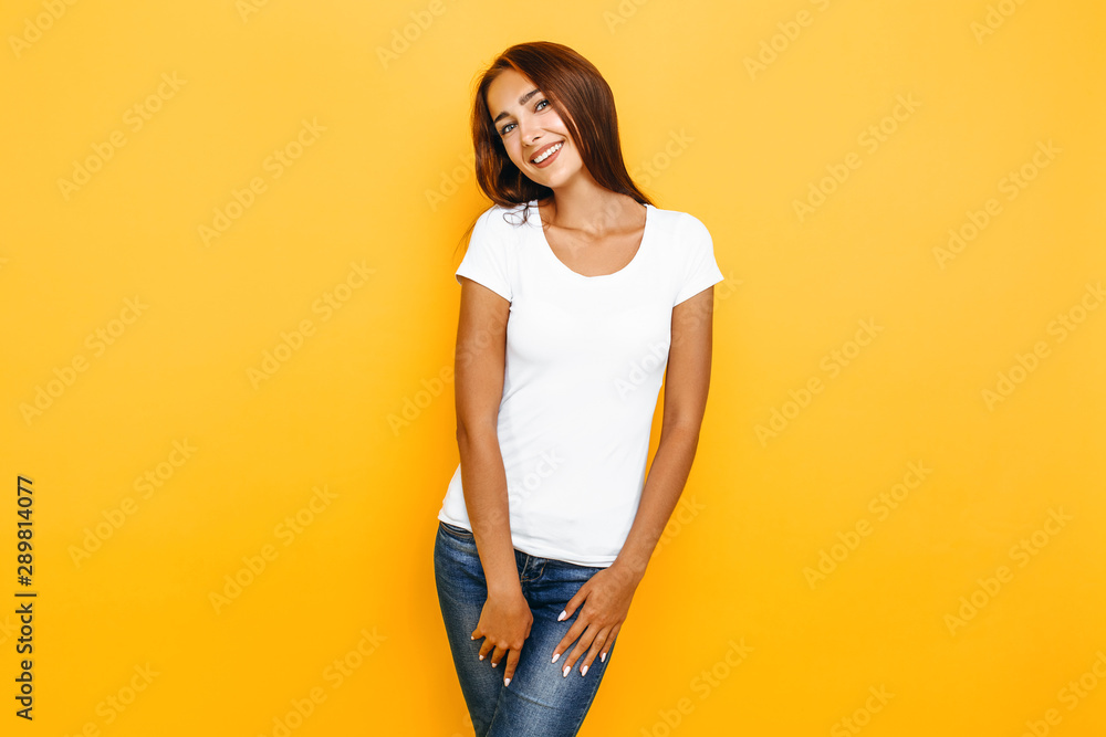Young beautiful woman in a white t-shirt posing on a yellow background - obrazy, fototapety, plakaty 