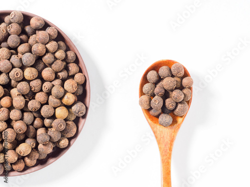 Allspice (Jamaica pepper) in clay plate and wooden spoon on white background