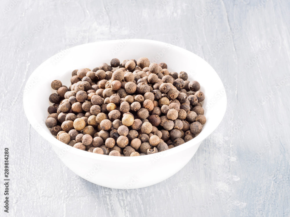Allspice (Jamaica pepper) in white cup on grey background Allspice (Jamaica pepper) in white cup on grey background
