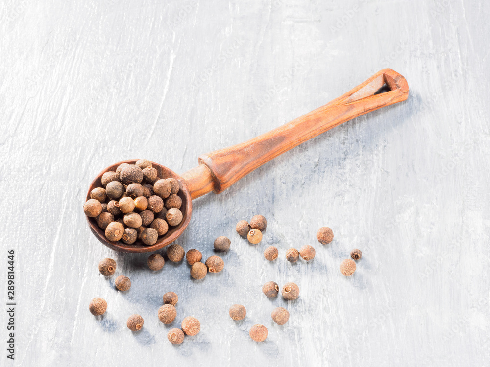 Allspice (Jamaica pepper) wooden spoon diagonally on grey cement background Allspice (Jamaica pepper) wooden spoon diagonally on grey cement background