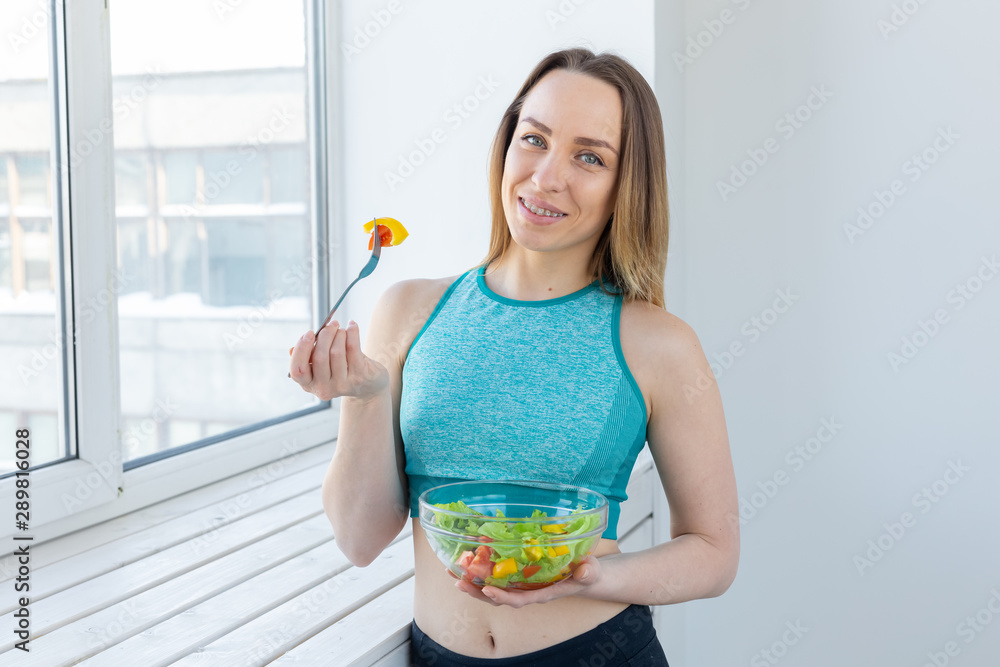 Healthy lifestyle, fitness and diet concept - dietary salad and slim woman in sports wear near window Healthy lifestyle, fitness and diet concept - dietary salad and slim woman in sports wear near window