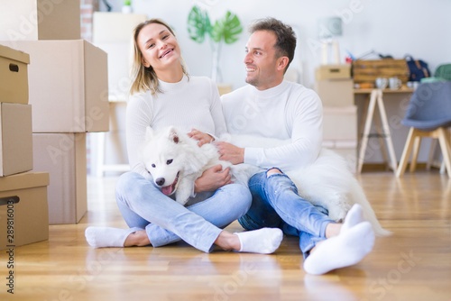 Fototapeta Naklejka Na Ścianę i Meble -  Young beautiful couple with dog sitting on the floor at new home around cardboard boxes