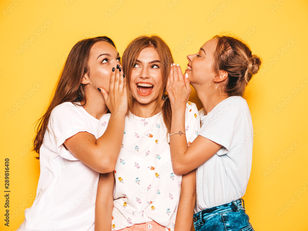 Three young beautiful smiling hipster girls in trendy summer clothes. Sexy carefree women posing near yellow wall in studio. Positive models going crazy and having fun.Share secrets, gossip Three young beautiful smiling hipster girls in trendy summer clothes. Sexy carefree women posing near yellow wall in studio. Positive models going crazy and having fun.Share secrets, gossip