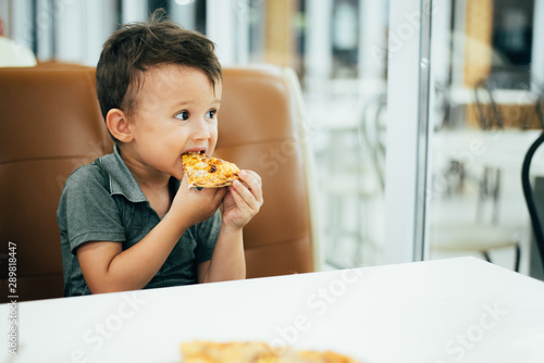 a little boy in a cafe or pizzeria sitting on the couch at the table and eats a piece of cut pizza, very tasty