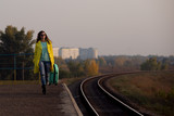 Girl tourist with a suitcase on a railway platform. girl in a yellow raincoat travels. Autumn train ride. Railway in the fall