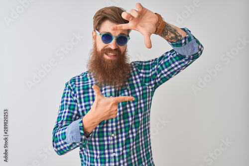 Young redhead irish man wearing casual shirt and sunglasses over isolated white background smiling making frame with hands and fingers with happy face. Creativity and photography concept.