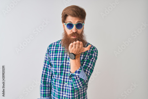 Young redhead irish man wearing casual shirt and sunglasses over isolated white background looking at the camera blowing a kiss with hand on air being lovely and sexy. Love expression.