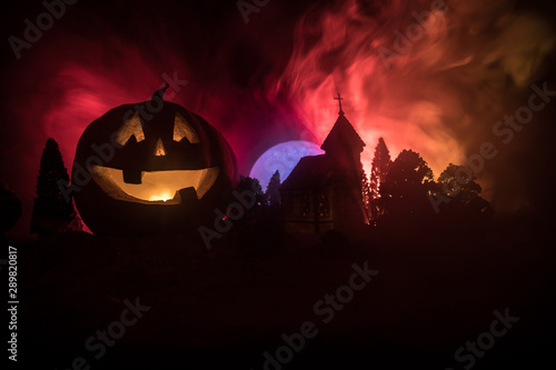 Horror view of Halloween pumpkin with scary smiling face. Head jack lantern with spooky building