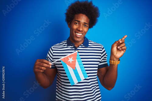 Young african american man holding Cuba Cuban flag standing over isolated blue background very happy pointing with hand and finger to the side