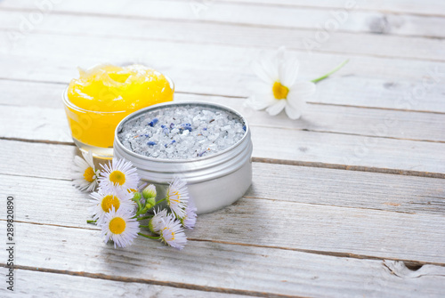 yellow calendula cream in glass pot  moisturizer and bath salt with white herbal flowers on weathered rusty wooden table background