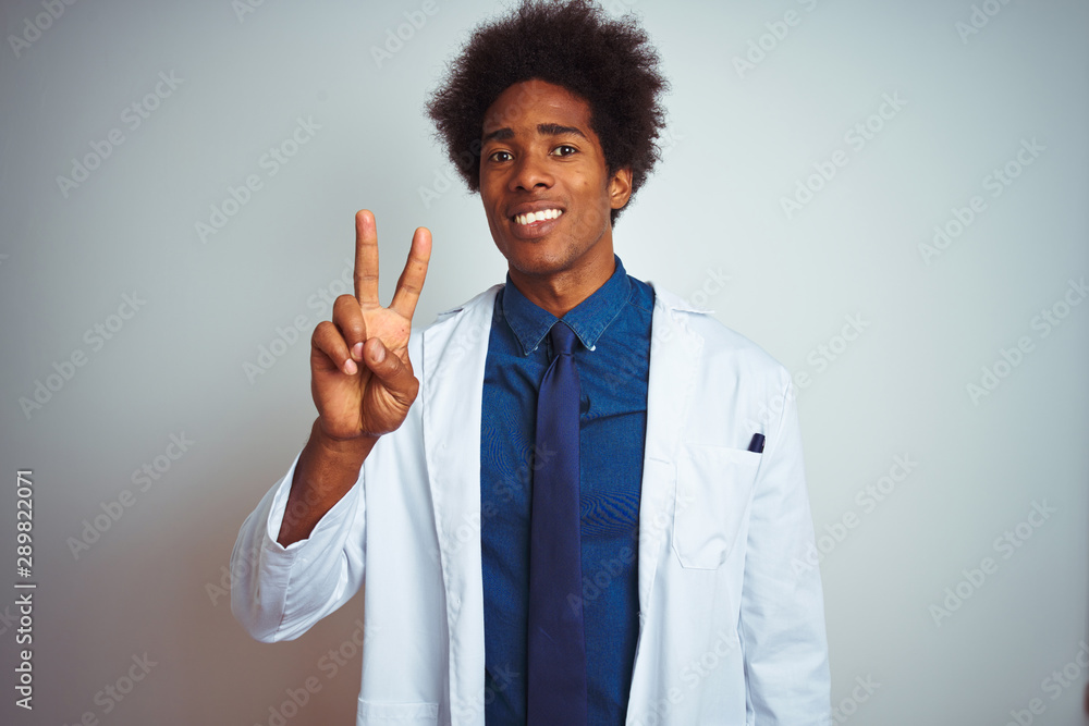 Young african american doctor man wearing coat standing over isolated white background showing and pointing up with fingers number two while smiling confident and happy.