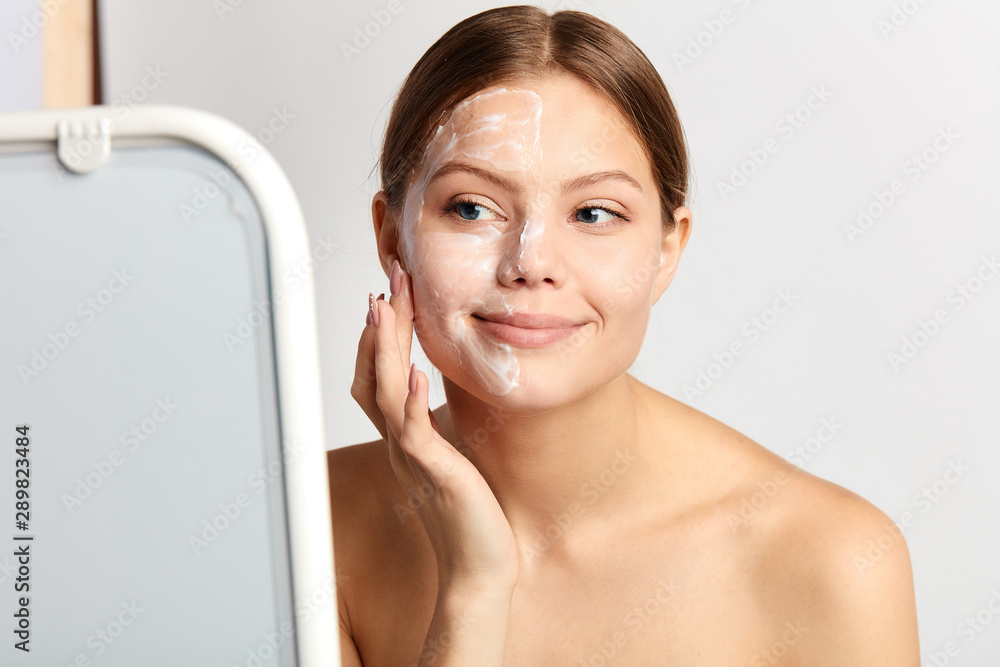 awesome cheerful nude girl massaging her face while standing behind the mirror. close up portrait. awesome cheerful nude girl massaging her face while standing behind the mirror. close up portrait.