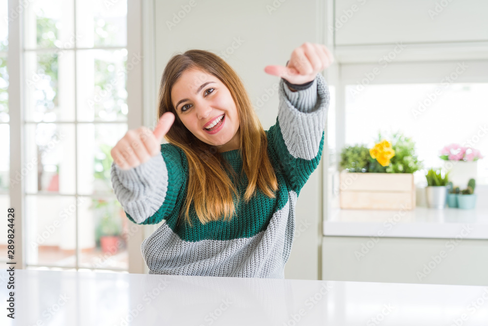 Young beautiful plus size woman wearing casual striped sweater approving doing positive gesture with hand, thumbs up smiling and happy for success. Winner gesture. Young beautiful plus size woman wearing casual striped sweater approving doing positive gesture with hand, thumbs up smiling and happy for success. Winner gesture.