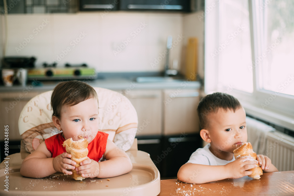 Brother and sister in the kitchen eating tubes with custard or protein cream Brother and sister in the kitchen eating tubes with custard or protein cream