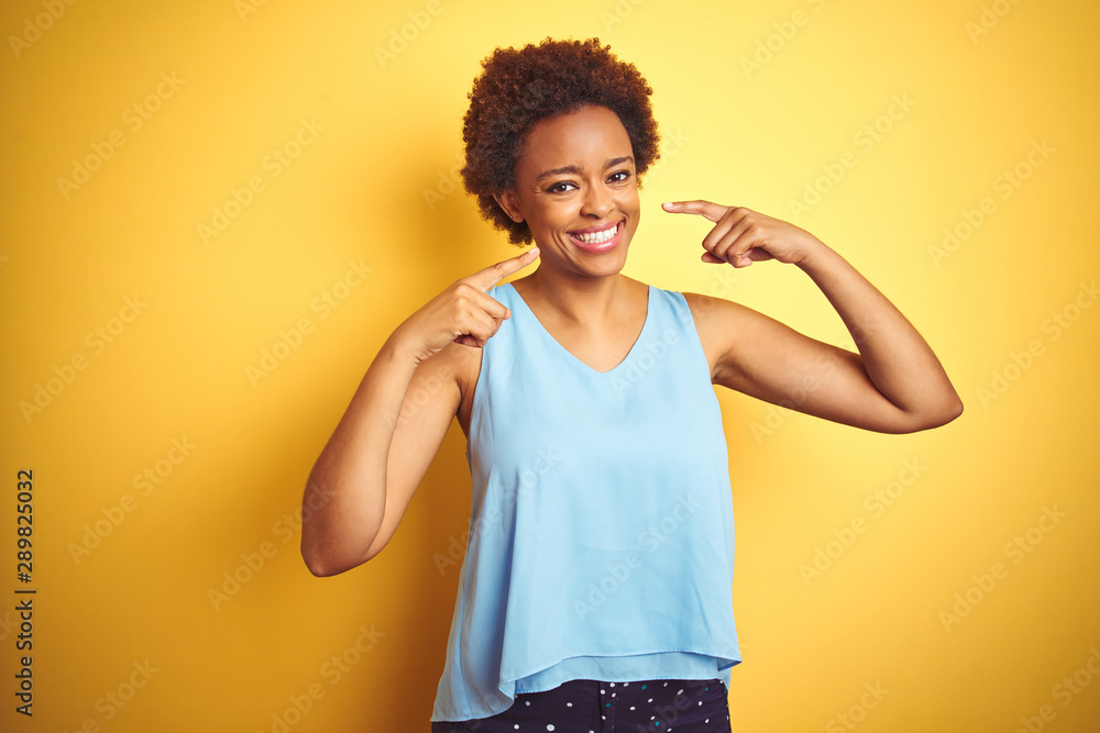 Beautiful african american woman wearing elegant shirt over isolated yellow background smiling cheerful showing and pointing with fingers teeth and mouth. Dental health concept. Beautiful african american woman wearing elegant shirt over isolated yellow background smiling cheerful showing and pointing with fingers teeth and mouth. Dental health concept.