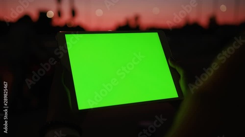 Close up young hands woman uses tablet computer with a horizontal green screen on night street amazing sunset internet map hold pc scroll smart phone social network tourist tracking blank chroma city