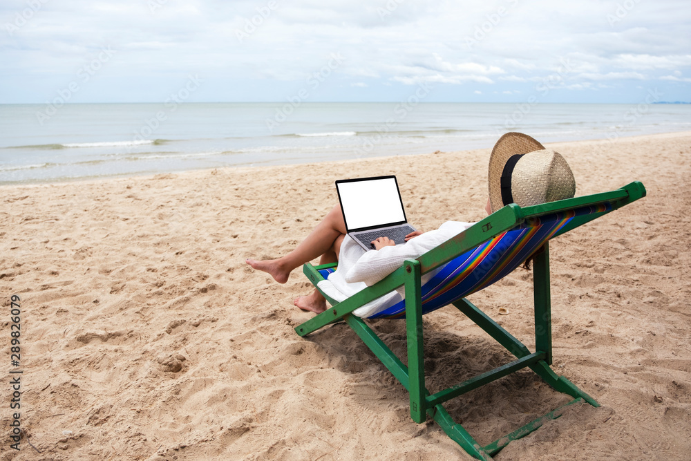 Mockup image of a woman using and typing on laptop computer with blank desktop screen while lying down on a beach chair Mockup image of a woman using and typing on laptop computer with blank desktop screen while lying down on a beach chair