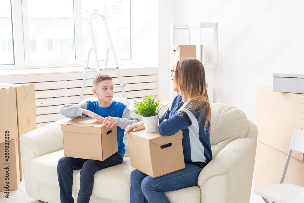 Cute single mom and little boy son sort boxes with things after the move. The concept of housewarming mortgage and the joy of new housing. Cute single mom and little boy son sort boxes with things after the move. The concept of housewarming mortgage and the joy of new housing.