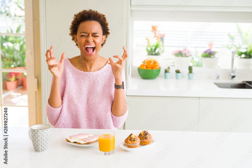 Young african american woman eating breaksfast in the morning at home celebrating mad and crazy for success with arms raised and closed eyes screaming excited. Winner concept Young african american woman eating breaksfast in the morning at home celebrating mad and crazy for success with arms raised and closed eyes screaming excited. Winner concept