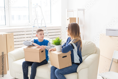 Cute single mom and little boy son sort boxes with things after the move. The concept of housewarming mortgage and the joy of new housing. © satura_