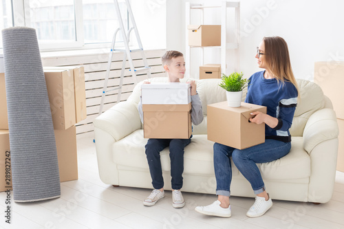 Cute single mom and little boy son sort boxes with things after the move. The concept of housewarming mortgage and the joy of new housing. © satura_