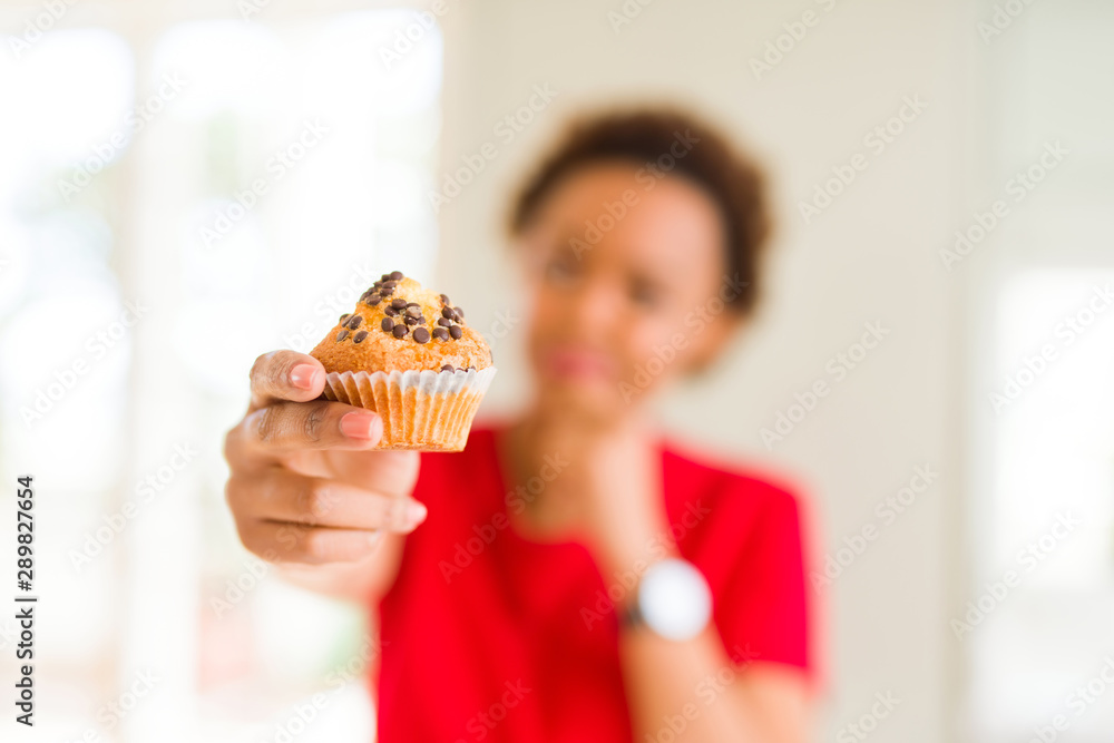 Young african american woman eating chocolate chips muffins serious face thinking about question, very confused idea Young african american woman eating chocolate chips muffins serious face thinking about question, very confused idea