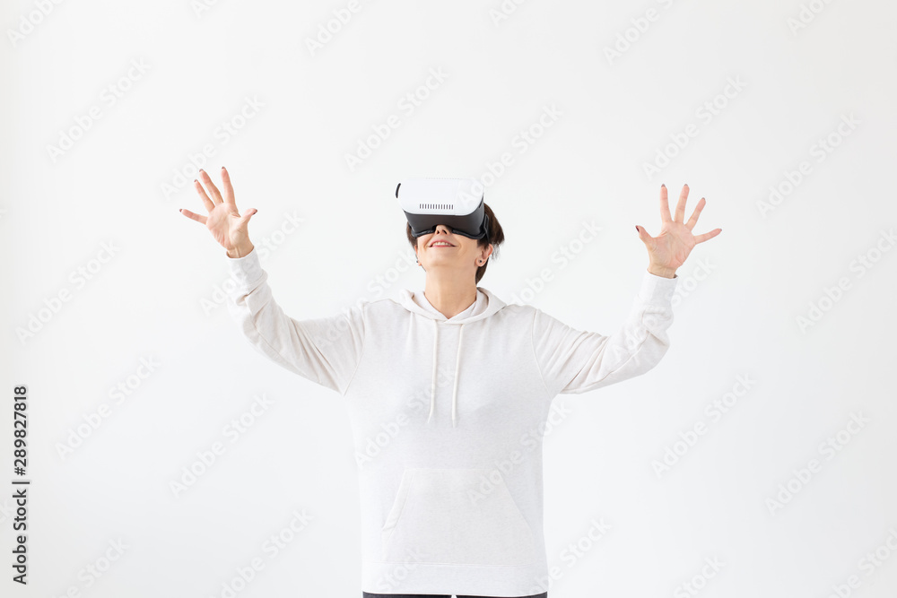 Unidentified middle-aged woman in a light sweater plays a 3D game with glasses of virtual reality on a white background. High technology concept for older people. Unidentified middle-aged woman in a light sweater plays a 3D game with glasses of virtual reality on a white background. High technology concept for older people.