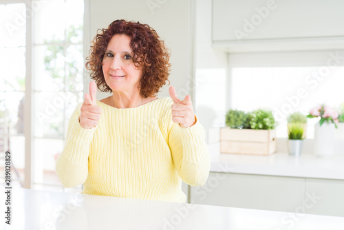 Beautiful senior woman wearing yellow sweater pointing fingers to camera with happy and funny face. Good energy and vibes.