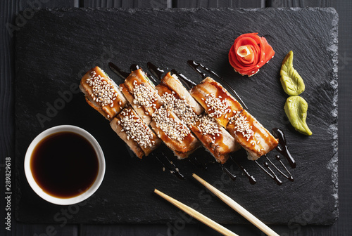 Sushi Set nigiri and sushi rolls in dark stone plate with soy sauce and chopsticks over black background.