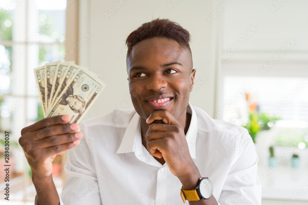 African american man holding twenty dollars bank notes serious face thinking about question, very confused idea African american man holding twenty dollars bank notes serious face thinking about question, very confused idea