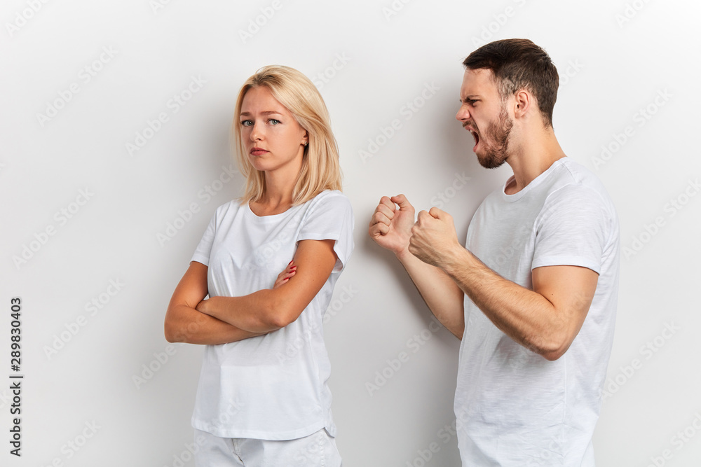 nervous man with clenched fists shouting at his wife, sad depressed crying woman standing with crossed arms she doesn't want to listen to her husband's hysterics. isolated white background nervous man with clenched fists shouting at his wife, sad depressed crying woman standing with crossed arms she doesn't want to listen to her husband's hysterics. isolated white background
