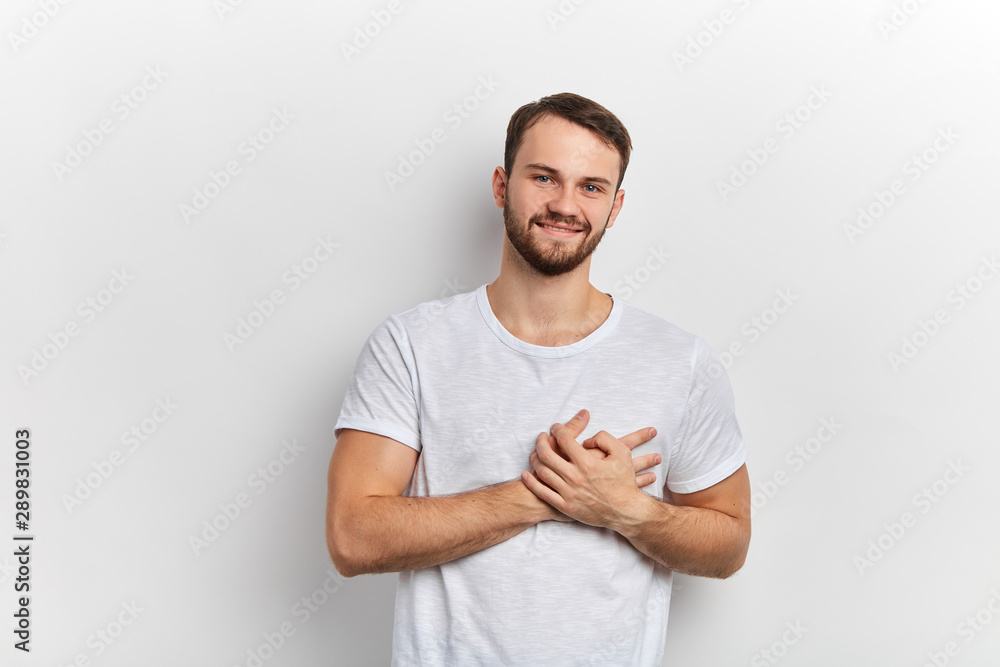 cheerful young man has friendly expression, keeps hands on heart, expresses his gratitude, shows love and great sympathy, isolated over white wall, positive feeling and emotion, body language cheerful young man has friendly expression, keeps hands on heart, expresses his gratitude, shows love and great sympathy, isolated over white wall, positive feeling and emotion, body language