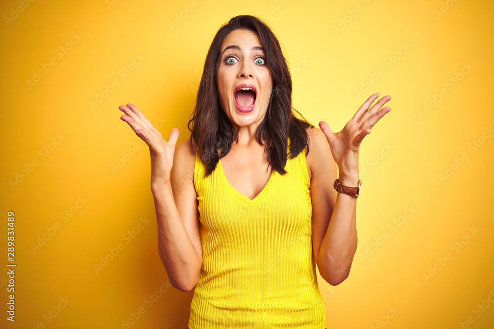 Young beautiful woman wearing t-shirt standing over yellow isolated background celebrating crazy and amazed for success with arms raised and open eyes screaming excited. Winner concept Young beautiful woman wearing t-shirt standing over yellow isolated background celebrating crazy and amazed for success with arms raised and open eyes screaming excited. Winner concept