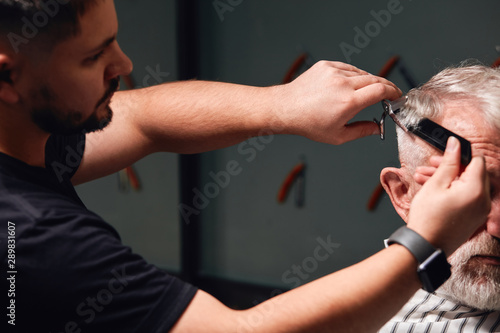 young talented barber doing new modern hairstyle for client. barber preparing old man for a date, party , event