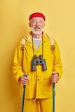 old tourist with binocular in stylish coat takes care of health, wellness, fitness, treatment. close up photo. isolated yellow background