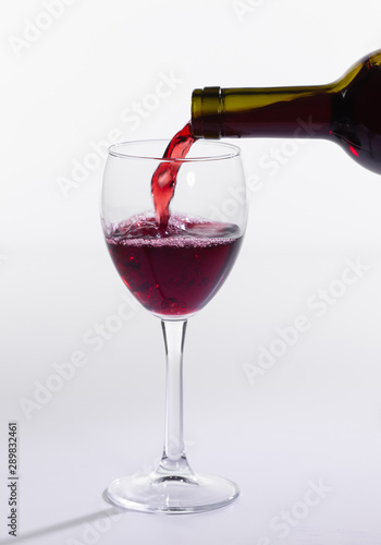 Red wine pouring from bottle into big glass on white