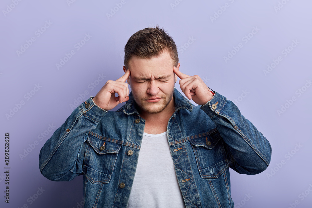 Portrait of weak unhealthy muscular man with closed eyes suffering from headache, touching temples with fingers isolated on blue background. close up portrait. Portrait of weak unhealthy muscular man with closed eyes suffering from headache, touching temples with fingers isolated on blue background. close up portrait.
