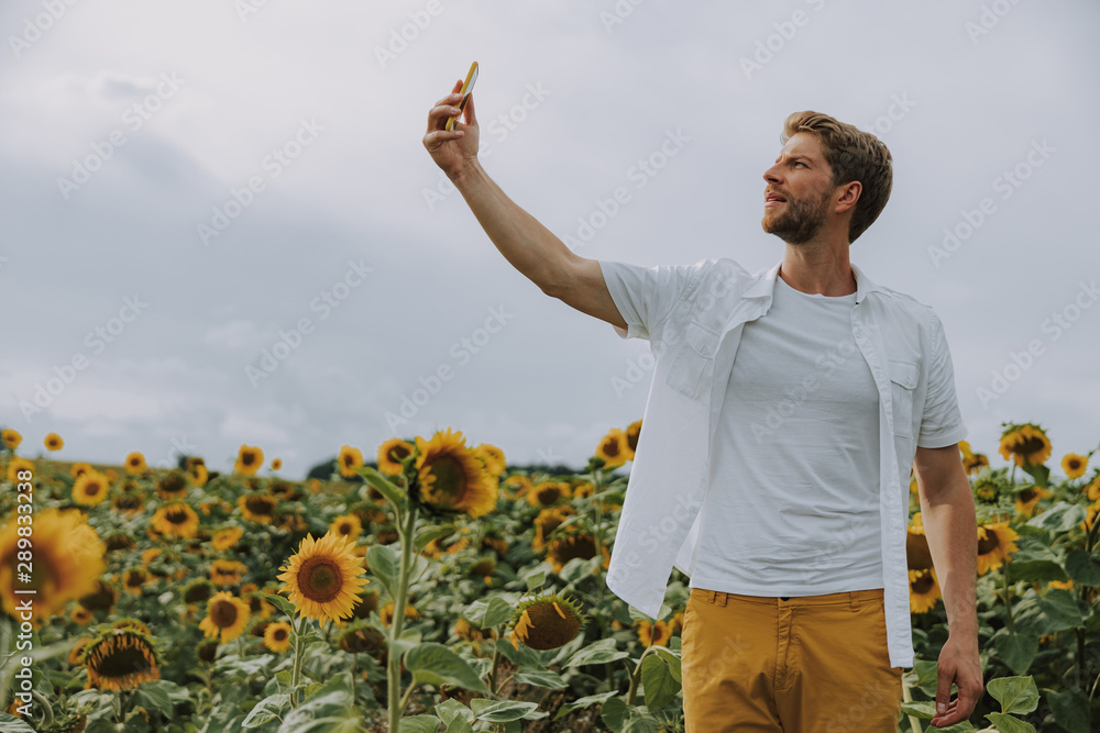 Happy Caucasian guy making selfie with phone in sunflower field