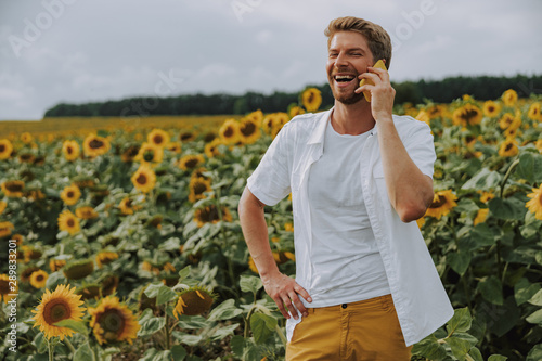 Happy Caucasian guy chatting on phone in sunflower field