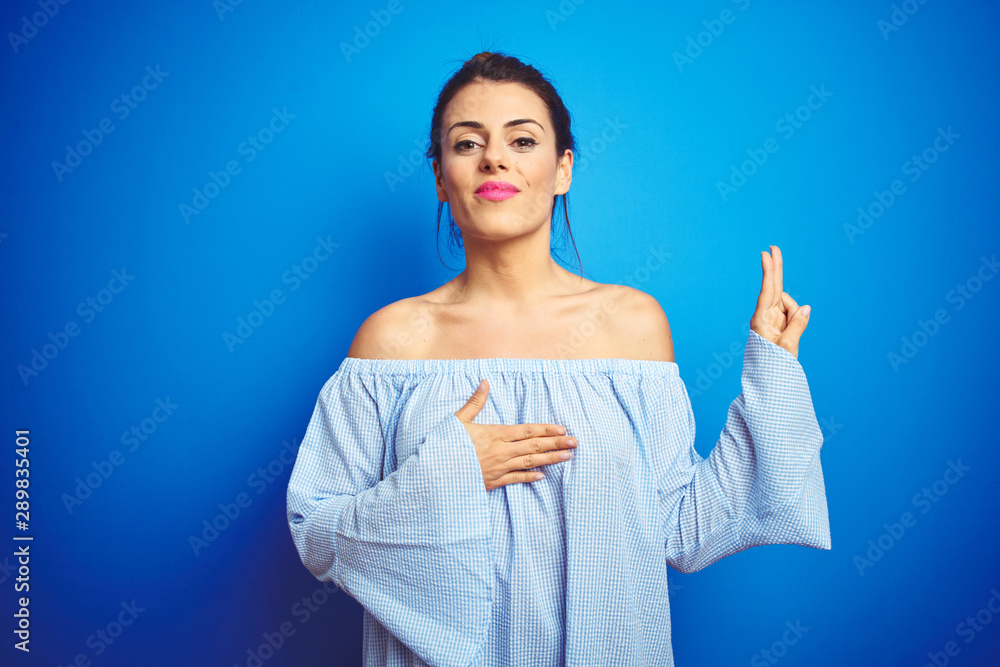 Fototapeta premium Young beautiful woman wearing bun hairstyle over blue isolated background smiling swearing with hand on chest and fingers up, making a loyalty promise oath
