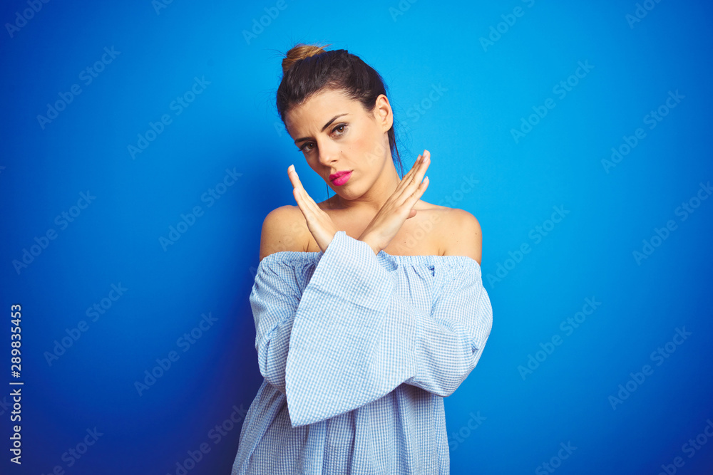 Young beautiful woman wearing bun hairstyle over blue isolated background Rejection expression crossing arms doing negative sign, angry face Young beautiful woman wearing bun hairstyle over blue isolated background Rejection expression crossing arms doing negative sign, angry face