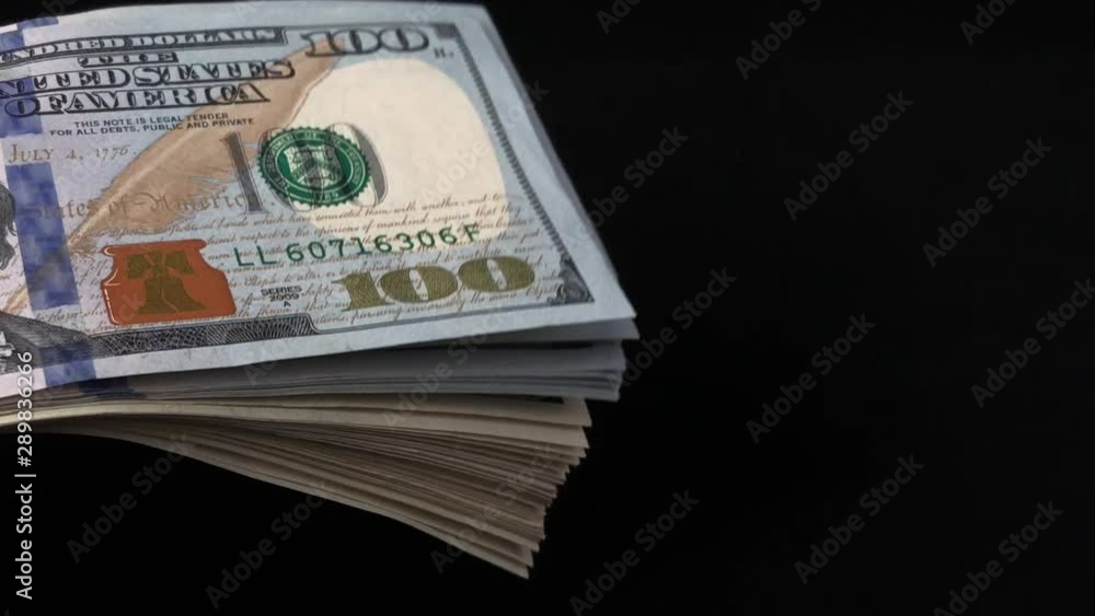 American dollars on a black background. In the hands of a person a bundle of American money. Many dollars move, close-up. Concept: wealth, enrichment, gain, income. American dollars on a black background. In the hands of a person a bundle of American money. Many dollars move, close-up. Concept: wealth, enrichment, gain, income.