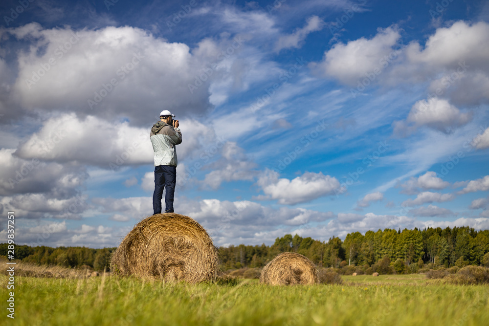 The photographer stands on a haystack in the field, makes a frame. Man in focus background blurred. The photographer stands on a haystack in the field, makes a frame. Man in focus background blurred.
