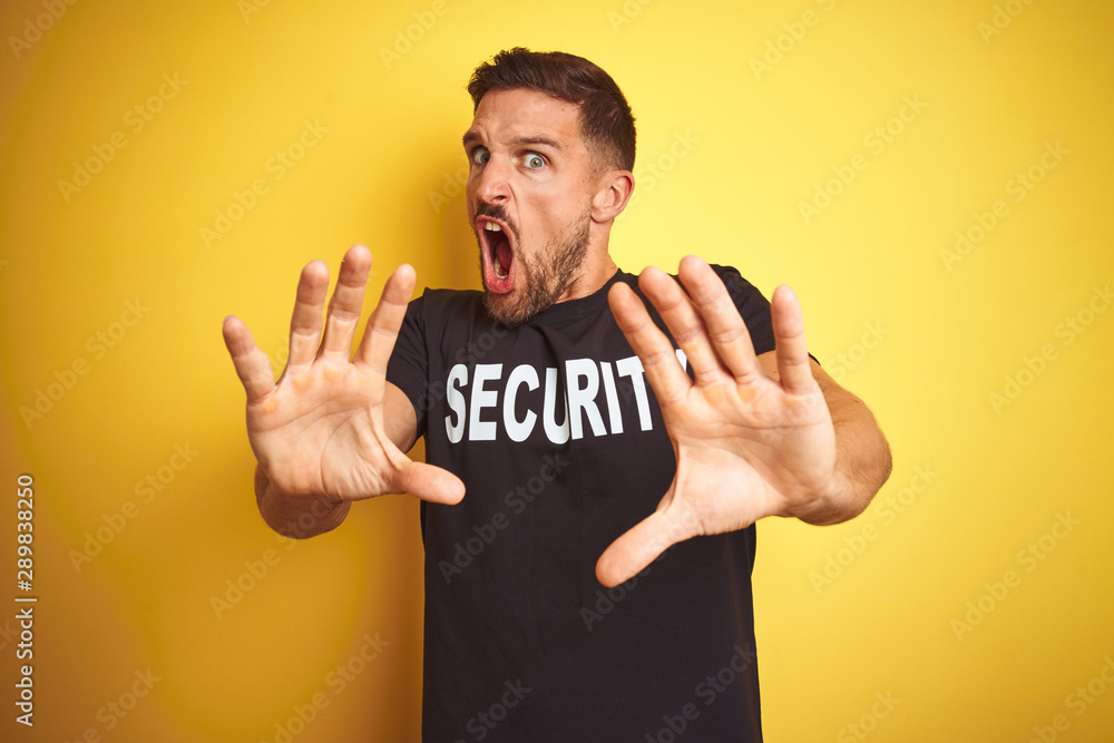 Young safeguard man wearing security uniform over yellow isolated background afraid and terrified with fear expression stop gesture with hands, shouting in shock. Panic concept. Young safeguard man wearing security uniform over yellow isolated background afraid and terrified with fear expression stop gesture with hands, shouting in shock. Panic concept.