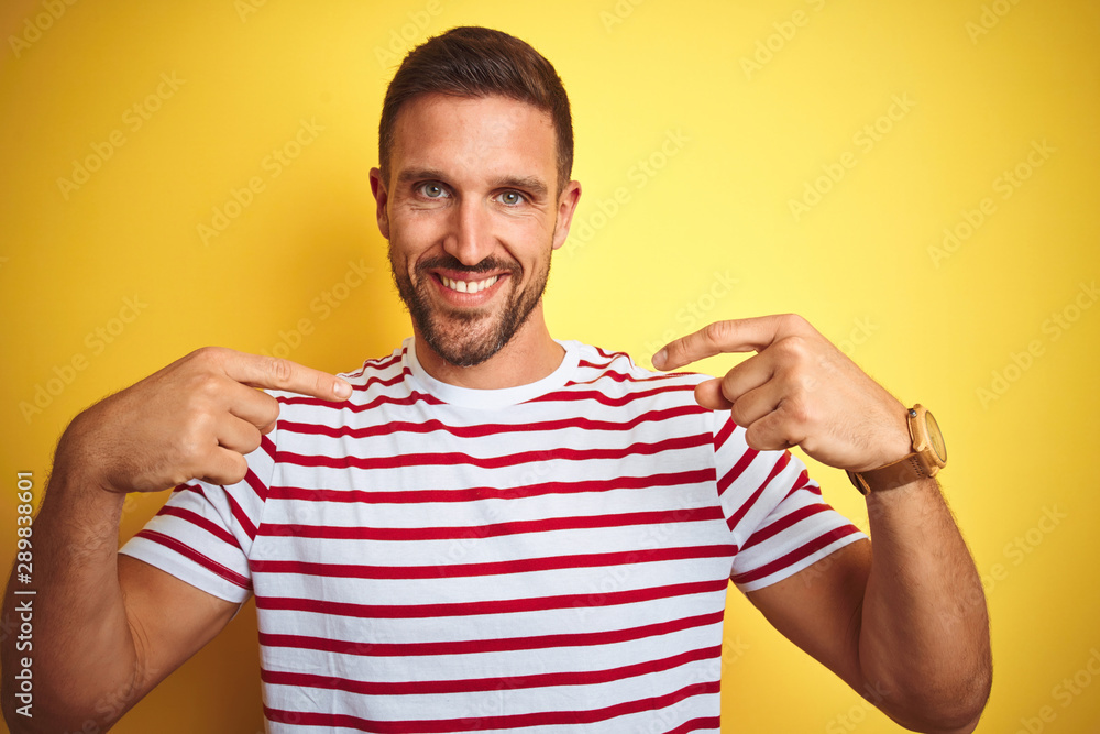 Young handsome man wearing casual red striped t-shirt over yellow isolated background looking confident with smile on face, pointing oneself with fingers proud and happy.