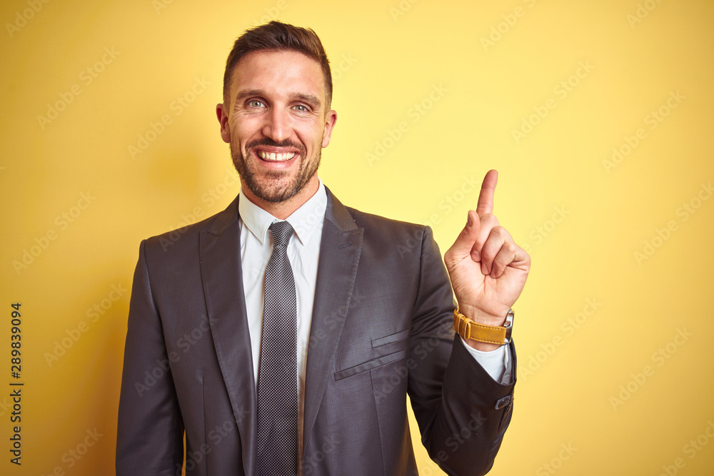 Young handsome business man over yellow isolated background with a big smile on face, pointing with hand and finger to the side looking at the camera. Young handsome business man over yellow isolated background with a big smile on face, pointing with hand and finger to the side looking at the camera.